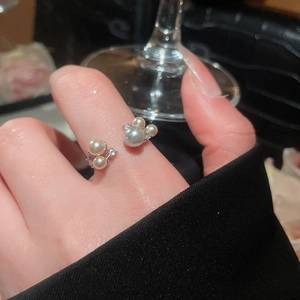 Detail view of vintage pearl open ring with zircons worn on finger with glass background