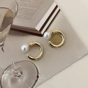 Detailed view of C-shaped gold-plated pearl earrings on an elegant tabletop setting