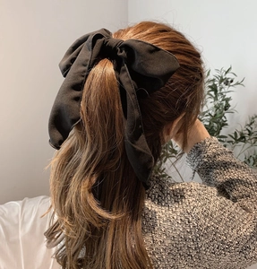 Close-up of a large black fabric bow hair tie styled on a model's ponytail with ribbons