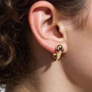 Cold style gold snake earrings with red gemstone eyes on a female model