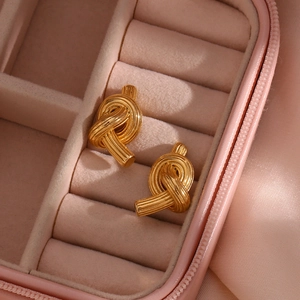 Golden knot earrings in a pink jewelry box, showcasing high-end brushed metallic details