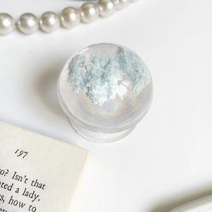Macro shot of transparent crystal ball phone stand with blue cloud interior on white table