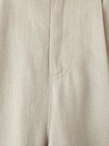 Detail of light beige linen trousers featuring precise stitching and clean placket design