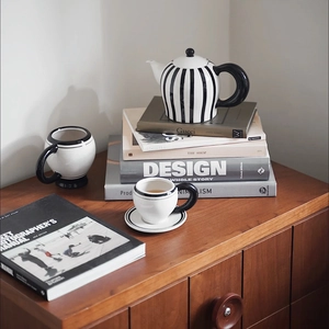 Minimalist black and white striped ceramic teapot with cups on a rustic wooden cabinet