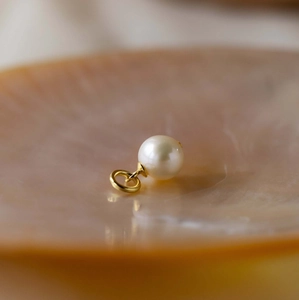 Close-up of a white pearl pendant with a 18K gold plated metal ring on a shell base
