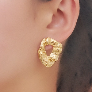 Close-up of gold irregular geometric hoop earrings with hammered metal texture on model