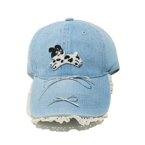 Détail de la casquette en denim bleu avec broderie chien, nœuds argentés et dentelle