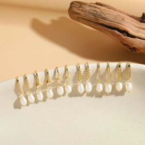 Macro display of twelve pairs of golden pearl earrings with cubic zirconia on wood