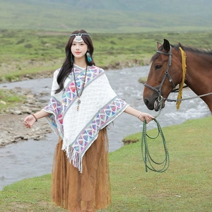 Ethnic knit poncho with colorful geometric patterns and tassels worn on scenic grassland
