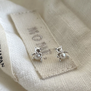 Detail of silver bear earrings with pearls on white cotton background with soft lighting