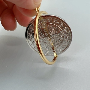 Macro detail of a spinning St. Benedict cross pendant in polished silver and gold metal
