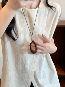 Detail of a minimalist wood resin oval pendant necklace on a beige linen texture sweater