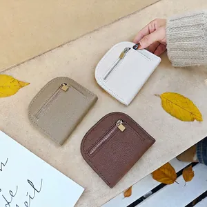 Three semi-circle pebble leather mini wallets in white, khaki and brown on stone background