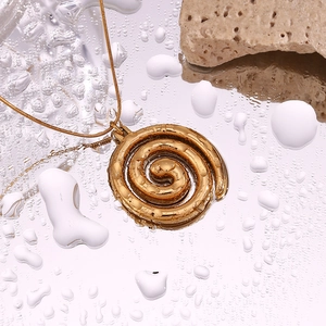Detailed macro shot of 18K gold plated swirl pendant necklace on reflective water droplets
