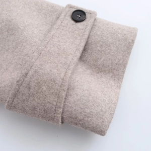 Detail shot of light beige wool coat cuff featuring a decorative strap and black button
