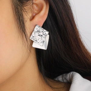 Close-up of double-layered geometric silver earrings with unique hammered metal texture