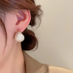 Détail de boucles d'oreilles géométriques blanc crème portées par un mannequin