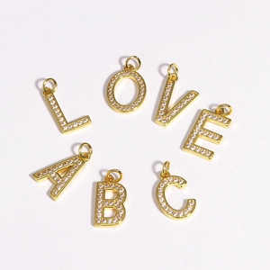 Detailed view of gold-plated letter charms with cubic zirconia inlay on white background