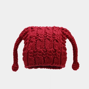Detail of red chunky knit beanie featuring cat ears and long braided earflaps with pom-poms