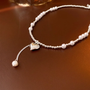Elegant silver heart pendant necklace with white pearls and beads on a leather surface