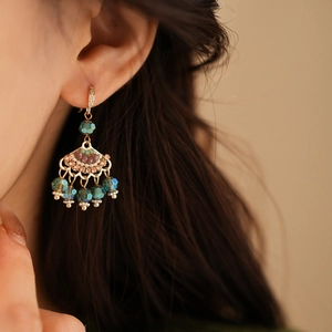Close-up of golden fan-shaped earrings with green zircon and pearl tassels on a model