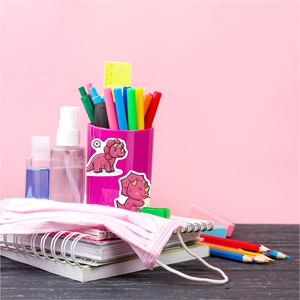 Close-up of pink dinosaur stickers on a pencil holder with school supplies background