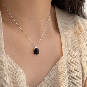 Close-up of black onyx pendant necklace with silver snake chain on a woman's neck