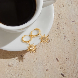 Detail of gold sun drop earrings with rhinestones next to a coffee cup with sun shadow