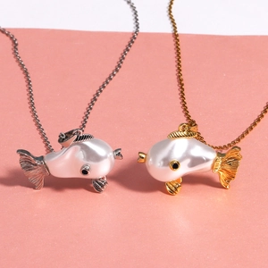 Macro shot of silver and gold fish-shaped pendants with white pearl bodies on a soft background
