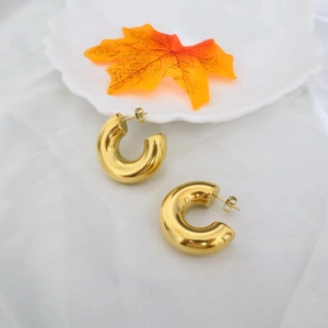 Minimalist 18k gold C-shaped hoop earrings displayed on white fabric with an autumn leaf