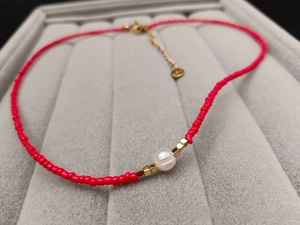 Detail of red seed bead necklace with white freshwater pearl on a velvet tray