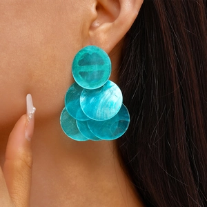Close-up of geometric layered turquoise round shell earrings worn by a female model