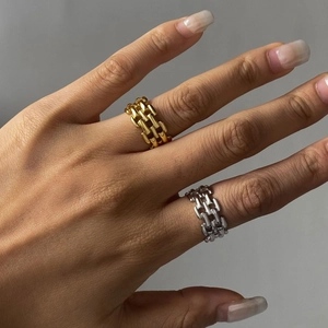 Detailansicht von Gold- und Silberkettenringen an der Hand auf grauem Hintergrund