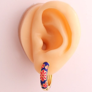 Golden enamel hoop earrings with deep blue floral pattern shown on a model ear