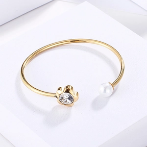 Detailed close-up of golden open bangle featuring a crystal flower and a white pearl accent