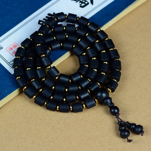 Détail de perles de bois noir avec intercalaires dorés et breloques gourde sur papier ancien