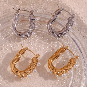 Macro shot of gold and silver U-shaped earrings with lava texture and white pearls