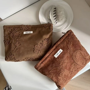 Vintage suede makeup bags with floral embroidery and wave patterns on a white surface