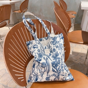 Detail of floral print canvas tote bag hanging on wooden chair in a cozy cafe setting