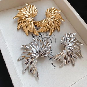 Macro detail of oversized pleated fan earrings in gold and silver metallic finishes