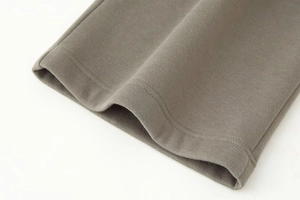 Detailed view of the double-stitched hem and taupe knit fabric texture on the garment
