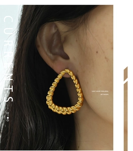 Close-up of golden teardrop earrings with twisted texture worn by a fashion model