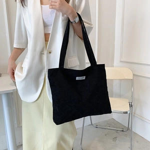 Detail showing black corduroy tote bag texture with white Fashion label on front