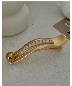 Detailed view of elegant gold metal hair clip with curved design and pearl decoration