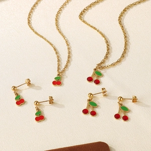 Set collana e orecchini a forma di ciliegia rossa con dettagli dorati su fondo neutro