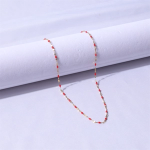 Detail of a thin gold stainless steel necklace with small red beads on a display prop