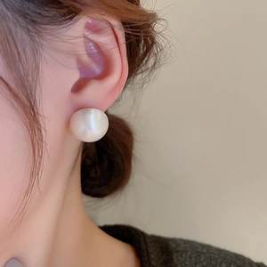 Close-up of minimalist round pearl stud earring worn on ear with golden metal plating