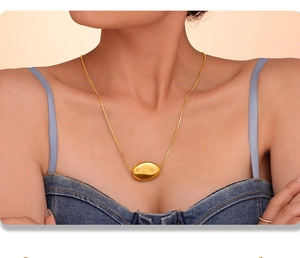 Close-up of a glossy gold bean pendant on a layered titanium steel necklace for women