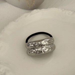 Close-up of a silver alloy hair tie with hammered rings on a white embossed plate