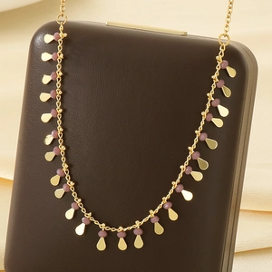 Close-up of golden tassel necklace with purple beads and teardrop pendants on a soft display